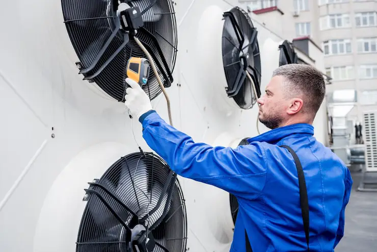A maintenance technician is checking a large outdoor HVAC condenser unit fan.