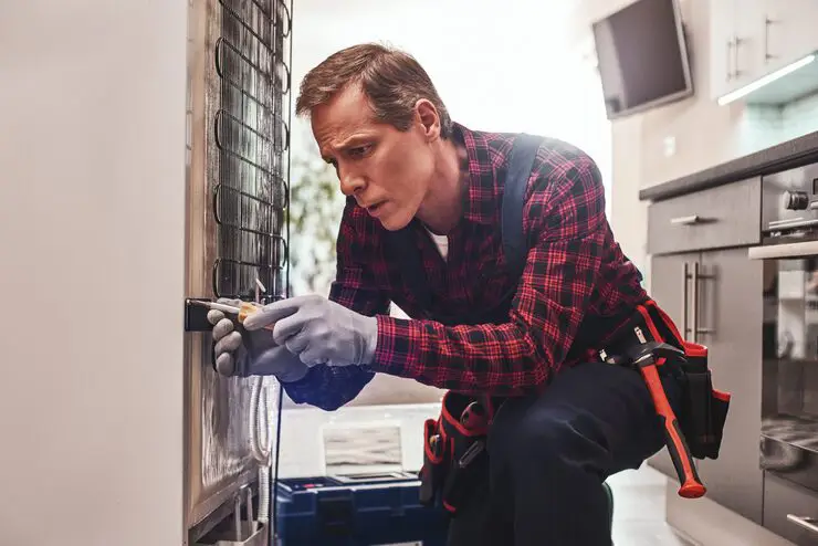 A repair technician focused on fixing the coils on the back of household appliance.