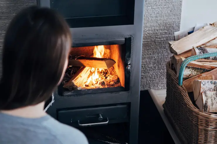 View from behind a woman looking into a black wood stove with a fire burning inside.