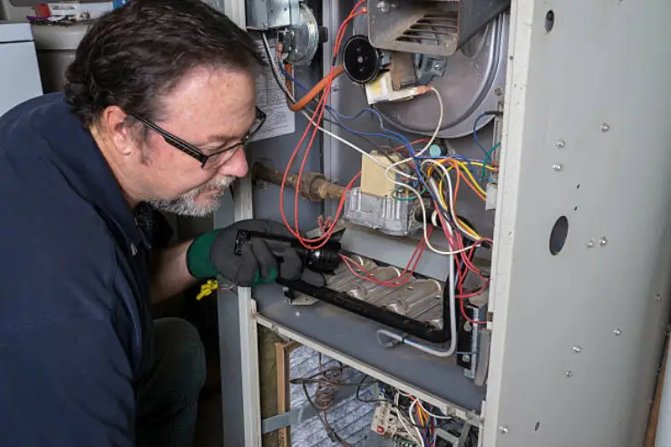 A heating technician performs maintenance on a large gas furnace in Ontario.
