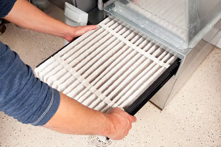 Person slides a clean, pleated furnace filter into the heating system.