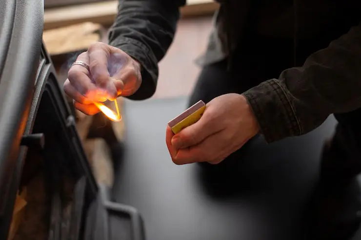 Close-up of hands lighting a match near a dark stove.