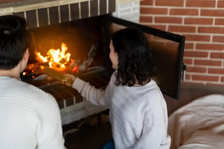 Two people tend to a brightly burning, open fireplace, highlighting home heating.