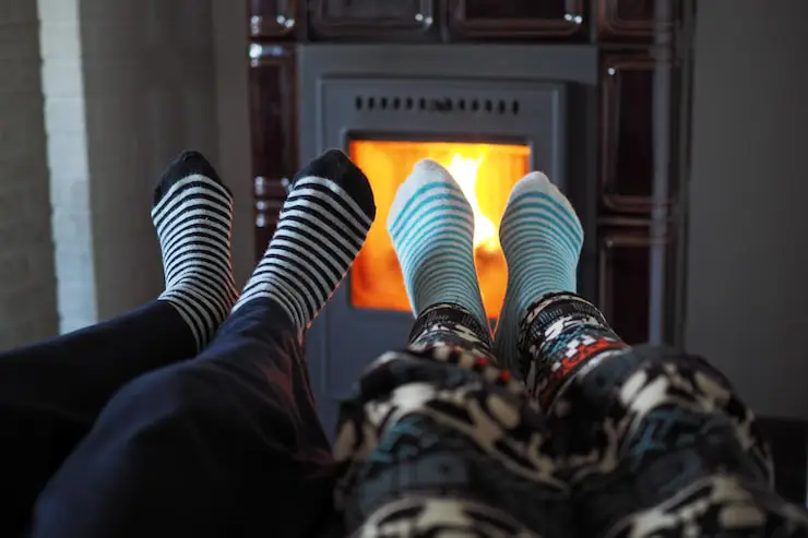 Two people's feet in warm socks relaxing by a cozy fireplace/furnace.
