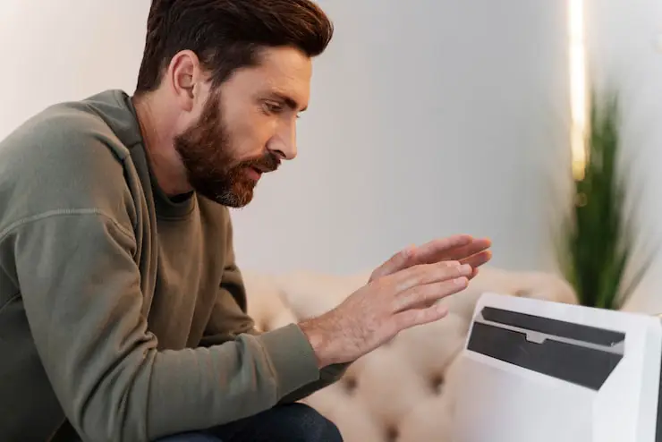 Man warming his hands by a portable electric heater.