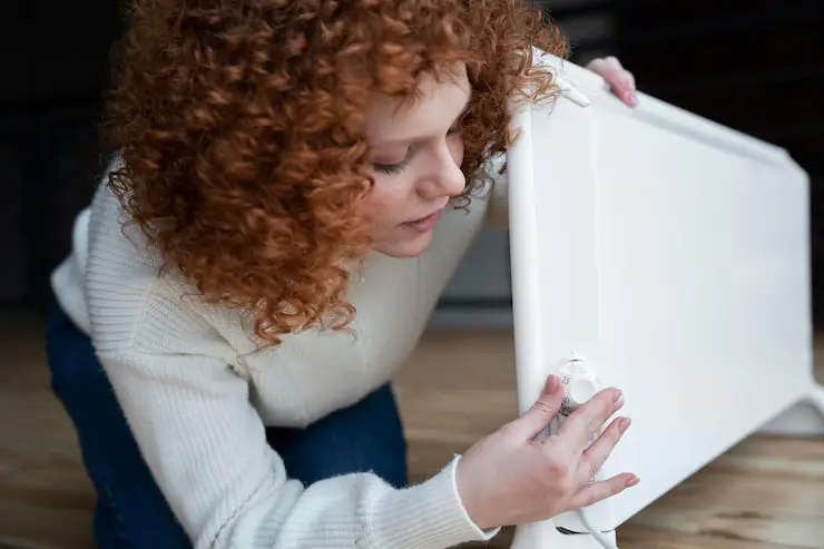 Woman adjusting dial on a white space heater.