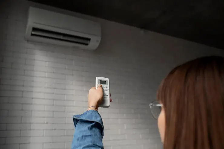 Woman using a remote control to adjust a wall-mounted mini-split AC/heat unit.