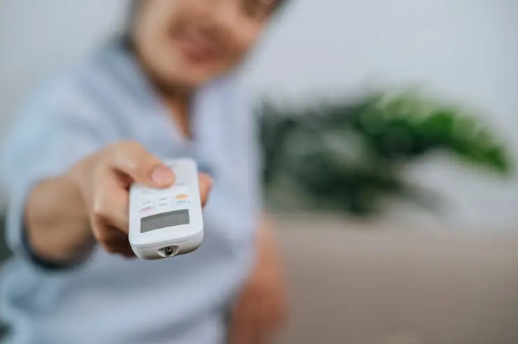 Person holding an HVAC remote control towards the camera, focused on the device.