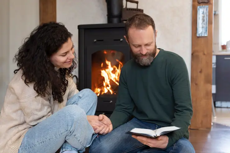Couple relaxing and reading by a warm Brock wood-burning stove.